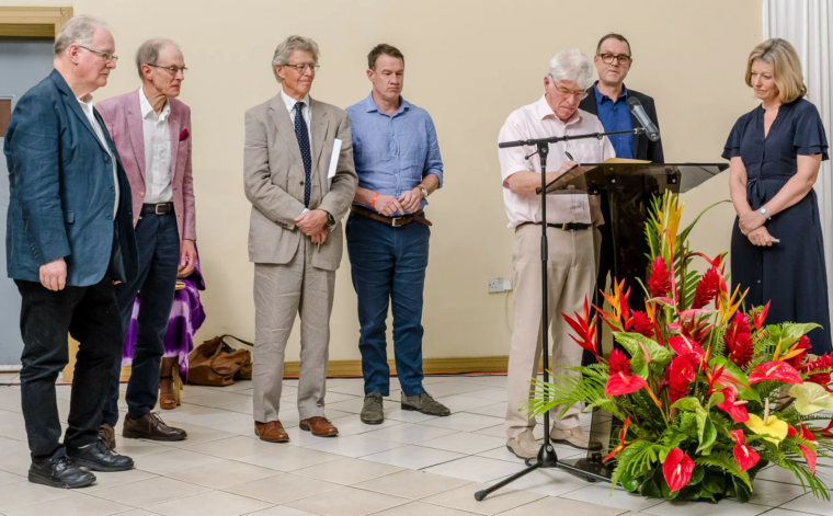 A family member stands at a podium at the apology ceremony while family members look on